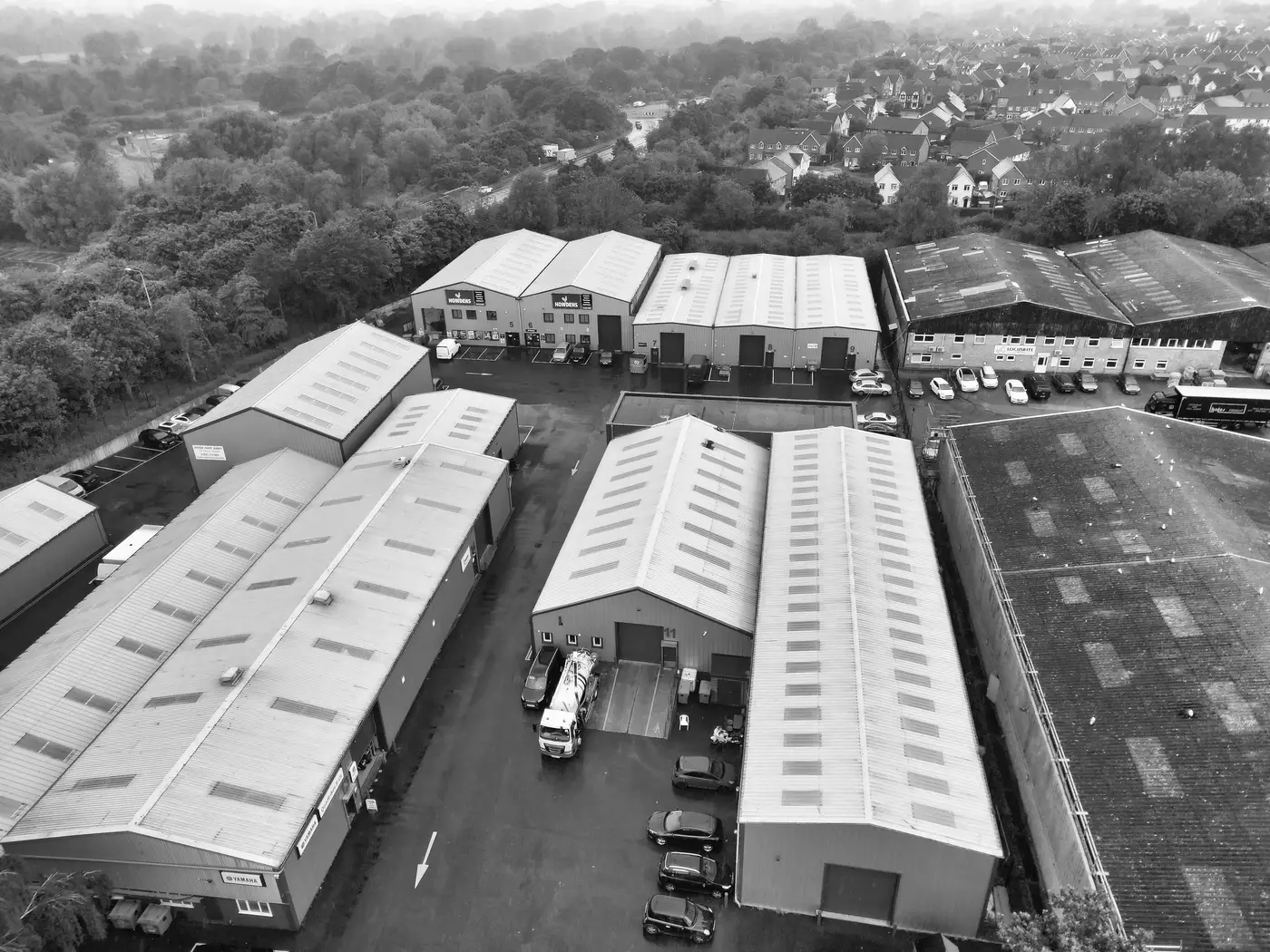 Black and white aerial view of several adjoining industrial warehouse units and a car park in Essex, England.