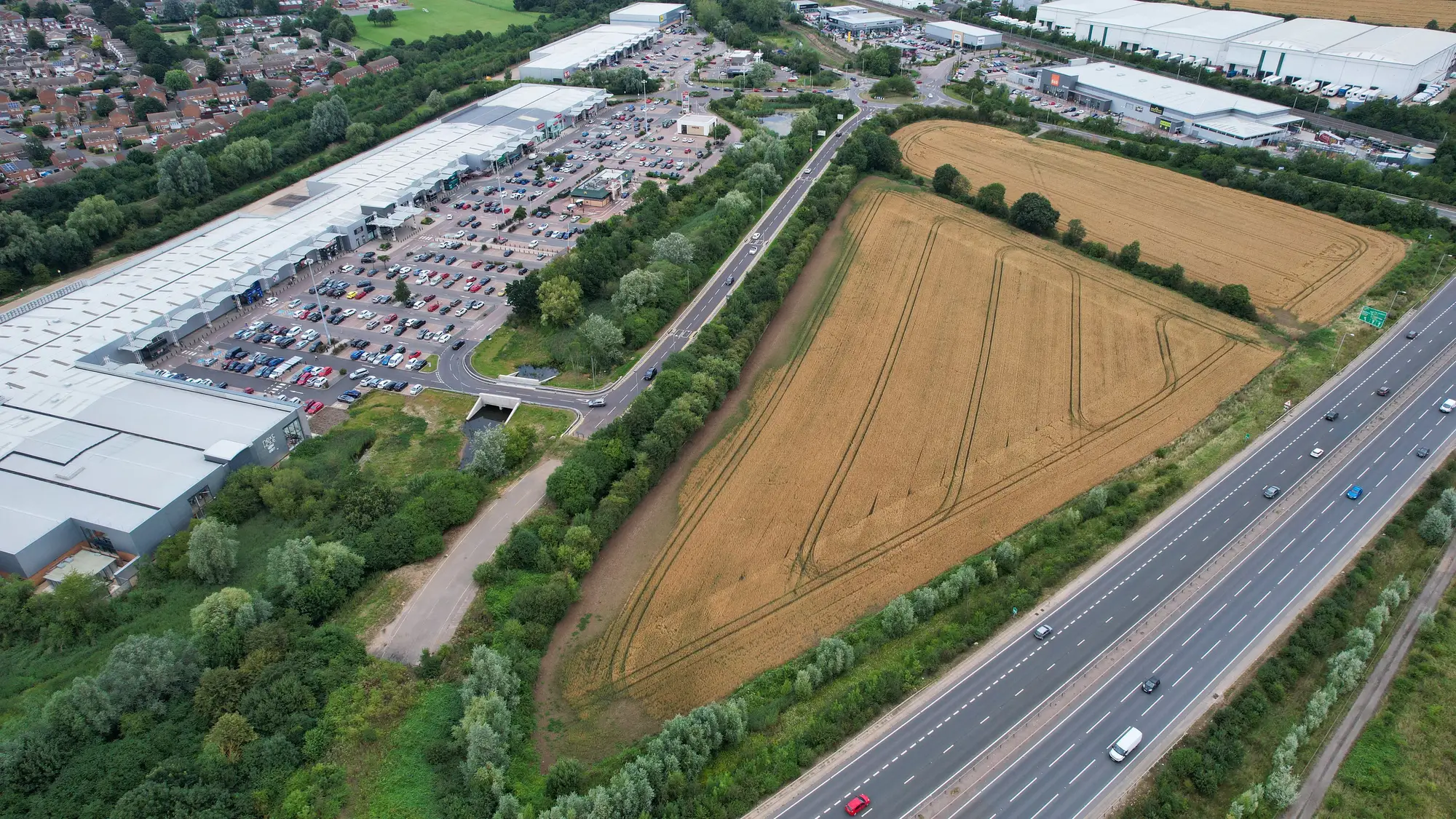 Aerial view of a retail park and its car park beside open fields and a motorway